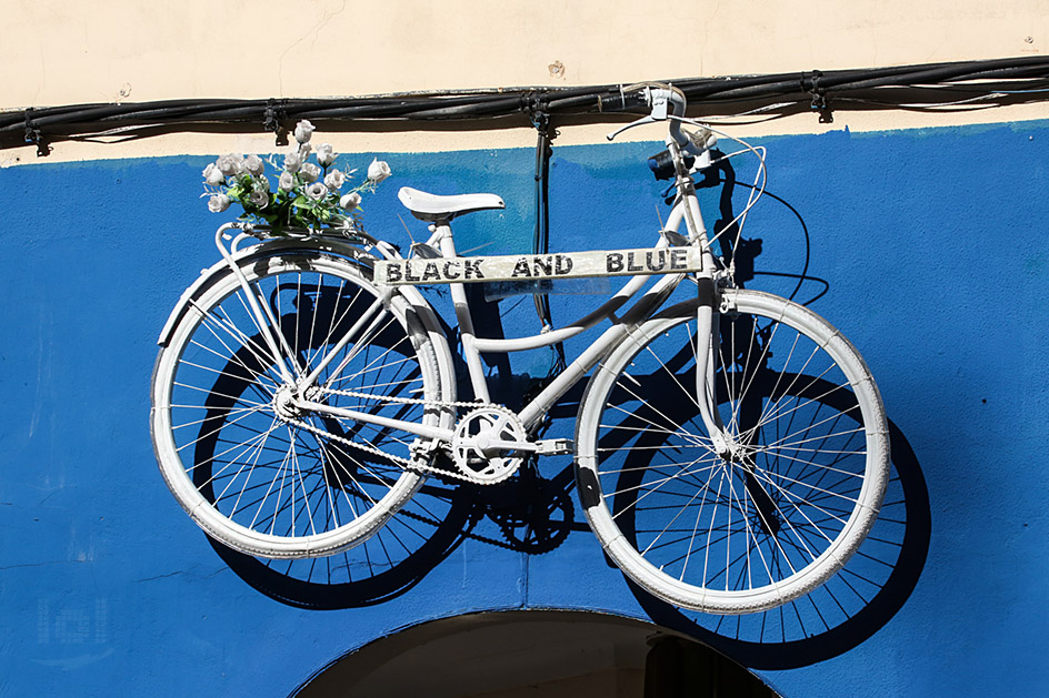 Ein weißes Fahrrad an einer blauen Hauswand als Werbeschild